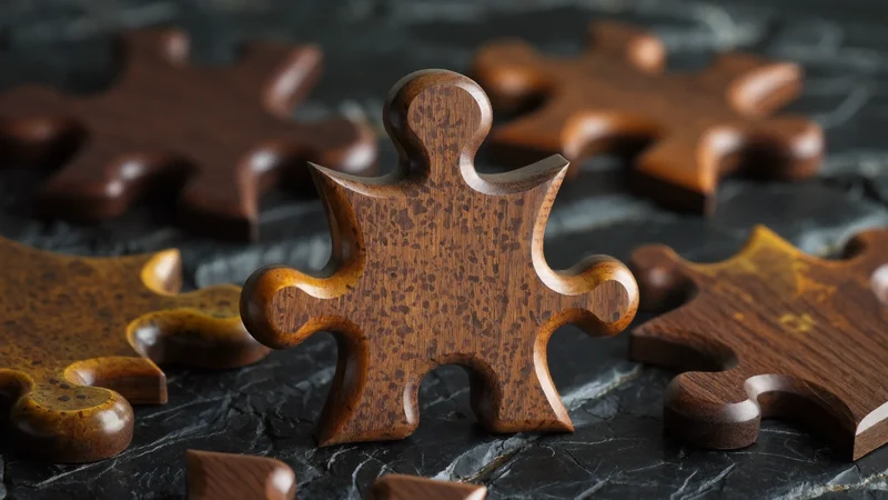 Drewniane elementy puzzli o fantazyjnych kształtach na ciemnej łupkowej powierzchni